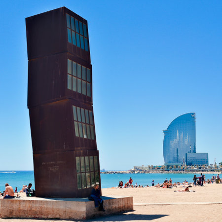 BARCELONA, SPAIN - MAY 7, 2017: Sunbathers at the Barceloneta Beach in Barcelona, Spain, with the COR-TEN steel sculpture designed by Rebecca Horn in the foreground and the W Hotel in the backgroundのeditorial素材