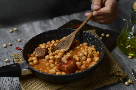 a frying pan with potaje de garbanzos, a spanish chickpeas stew with chorizo and serrano ham, on a rustic wooden tableの写真素材