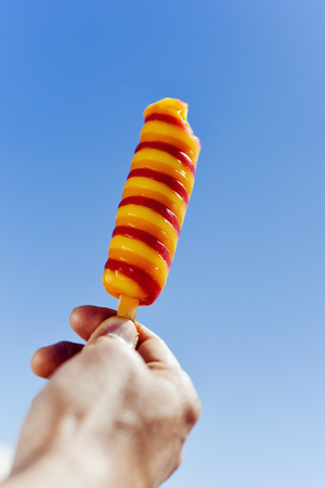 closeup of a refreshing ice pop in the hand of a young caucasian man against the blue skyの写真素材