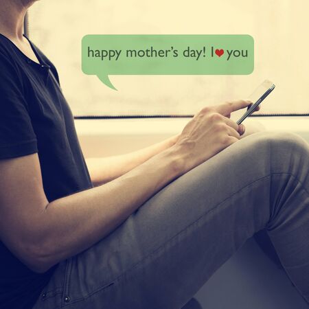 closeup of a young caucasian man in a train or a subway writing a text message with his smartphone to congratulate his mother, with the text happy mothers day, I love youの写真素材