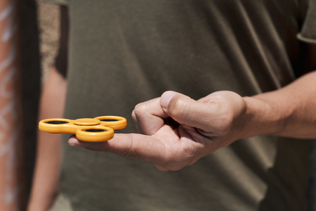 closeup of a young caucasian man playing with a yellow fidget spinner in the streetの写真素材