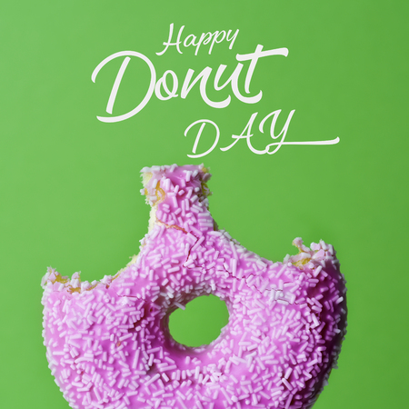 a nibbled appetizing donut coated with a pink frosting and white sprinkles and the text happy donut day against a bright green backgroundの写真素材