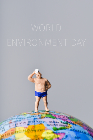 miniature man wearing swimsuit and drying his forehead with a handkerchief on the top of the terrestrial globe and the text world environment dayの写真素材
