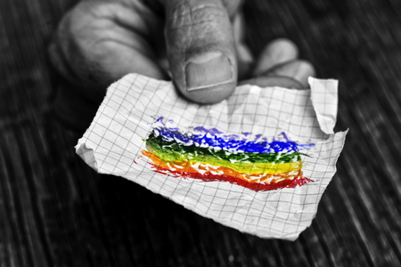 closeup of a young caucasian man in black and white with a piece of paper in his hand with a colorful rainbow flag painted in itの写真素材