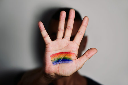closeup of a young caucasian man with the palm of his hand in front of his face with a rainbow flag...