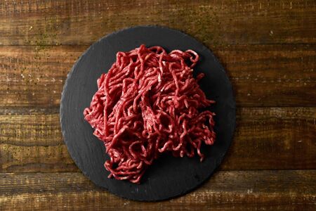 high-angle shot of a pile of raw beef ground meat on a slate plate, placed on a rustic wooden tableの写真素材