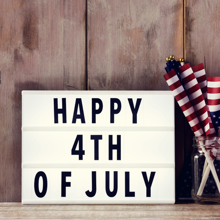 a lightbox with the text happy 4th of july and some american flags on a glass jar, on a rustic wooden backgroundの写真素材
