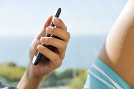 closeup of a young caucasian man in swimsuit using a smartphone outdoors, with the ocean in the backgroundの写真素材