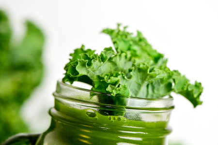 a kale smoothie served in a mason jar topped with a leaf of kale, on a white backgroundの写真素材