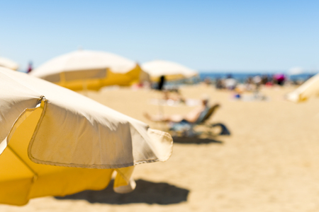 closeup of some beige umbrellas and in a beach in the Mediterranean sea, with many unrecognizable people sunbathing in the backgroundの写真素材