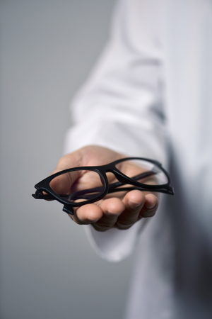 closeup of a young optician man in a white coat bringing a pair of eyeglasses to the observerの写真素材