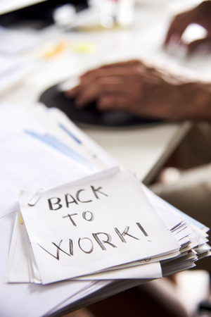closeup of a man sitting at his office desk and a note in the foreground with the text back to work handwritten in itの写真素材