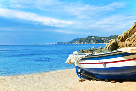 an old fishing boat stranded in the quiet beach Platja de Sa Caleta in Lloret de Mar, in the Costa Brava, Spainの写真素材