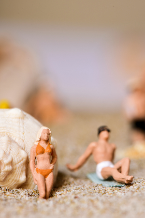 a miniature woman and a miniature man wearing swimsuit on the sand of the beach, with a negative space on topの写真素材