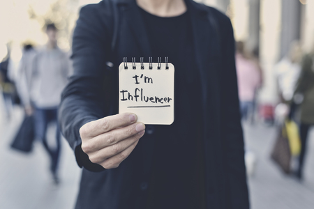 closeup of a young caucasian man in the street showing a spiral notepad with the text I am influencer written in itの写真素材
