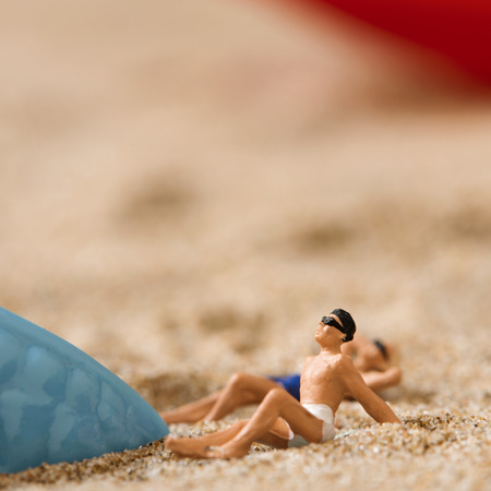 miniature man and miniature woman wearing swimsuit relaxing next to a blue plastic starfish on the sand of the beachの写真素材