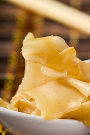 closeup of some slices of pickled ginger in a white ceramic bowl, on a table set for lunch or dinnerの写真素材