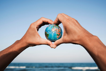 closeup of a young caucasian man with a world globe in his hands forming a heart against the blue...
