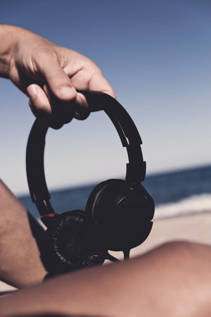 closeup of a young man holding a pair of headphones in his hand sitting in the sand of the beach