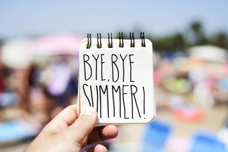 closeup of a young man in the beach showing a spiral notepad with the text bye bye summer handwritten in itの写真素材