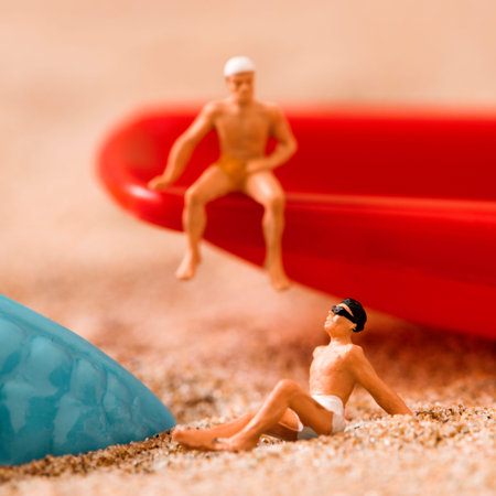 two different miniature men wearing swimsuit relaxing next to a blue plastic starfish and a red toy...