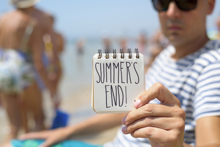 closeup of a young man in the beach showing a spiral notepad with the text summers end handwritten in itの写真素材