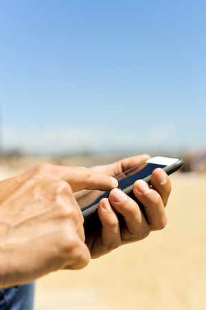 closeup of a young caucasian man using a smartphone next to the beach, with a negative space on topの写真素材