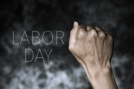 closeup of the raised fist of a young man against a gradient dark gray background and the text labor dayの写真素材