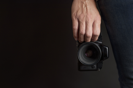 closeup of a young caucasian man with a reflex camera in his hand against a dark background with a negative space on the leftの写真素材