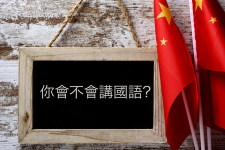 a wooden-framed chalkboard with the question do you speak Chinese? written in Chinese, and some flags of China against a rustic wooden backgroundの写真素材