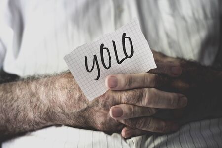 closeup of an old caucasian man with a note in his hands with the word yolo, for you only live once, written in itの写真素材