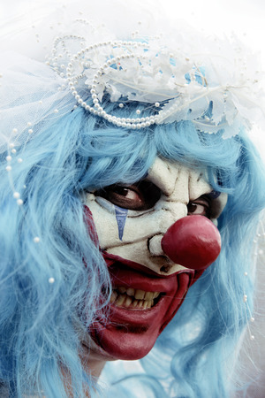 closeup of a scary evil clown wearing a dirty and ragged bride dress outdoorsの写真素材