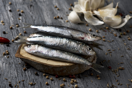 closeup of some raw sardines on a gray rustic wooden table sprinkled with peppercornsの写真素材