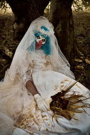 a scary evil clown wearing a dirty and ragged bride dress and bridal bouquet with wilt flowers,...