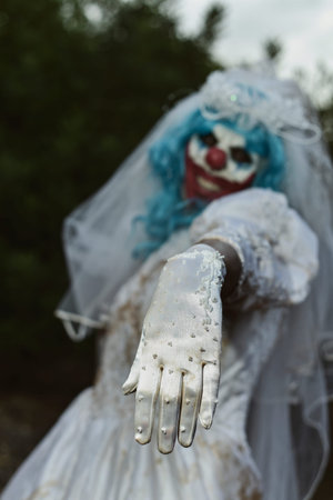 a scary evil clown wearing a dirty and ragged bride dress in a disturbing rural landscape at night
