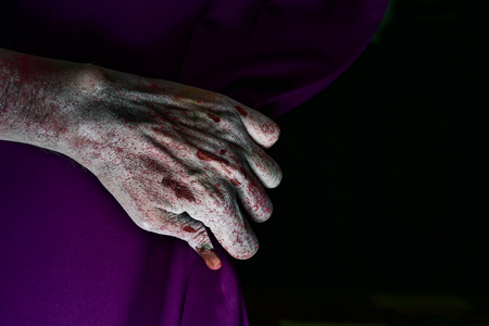 closeup of the scary hand of an undead man drawing a purple stage curtain, with a blank black background in the backgroundの写真素材
