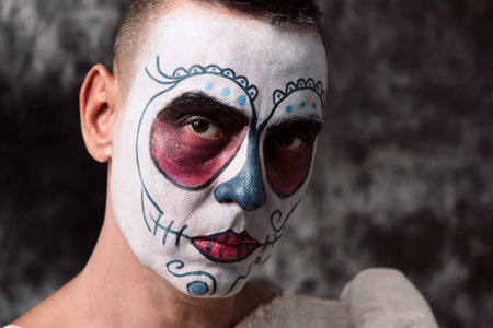 closeup of a person with short hair in a bride dress with a mexican calaveras makeup, against a dark...