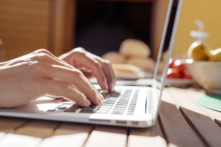 closeup of a young caucasian man using a laptop sitting at a wooden table outdoors during a mealの写真素材