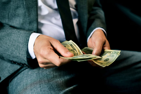a young caucasian man in an elegant gray suit counts dollar bills sitting in the back seat of a car