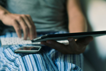 closeup of a young caucasian man in pajamas sitting in a comfortable armchair using a smartphone, a...