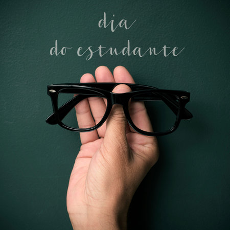 a pair of black plastic-rimmed eyeglasses in the hand of a young man and the text dia do estudante,...