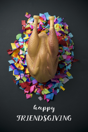 high-angle shot of a rubber roast turkey on a pile of confetti, placed on a rustic surface, and the text happy friendsgivingの写真素材