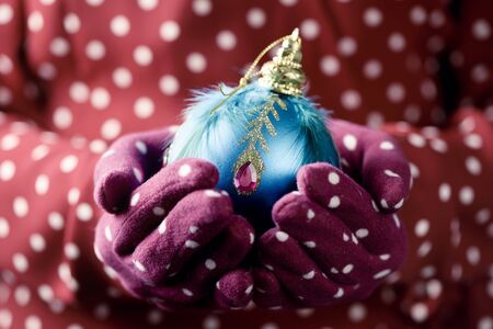 closeup of a caucasian woman wearing a pair of red gloves patterned with white dots holding an ornamented christmas ball in her handsの写真素材