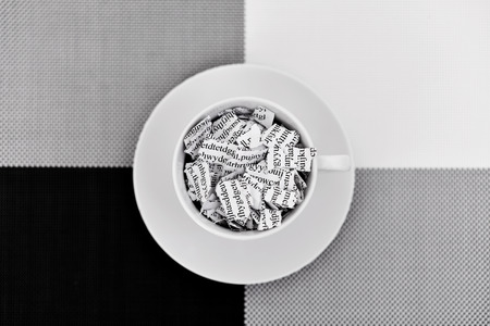 a printed letter or document broken into a thousand pieces in a white ceramic coffee cup placed on a black, gray and white backgroundの写真素材