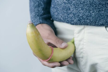 closeup of the a young caucasian man holding a banana with a pink condom in it in front of his crotchの写真素材