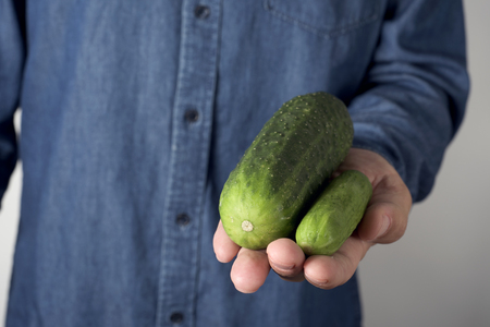 closeup of a young man holding a big cucumber next to a smaller one in his handの写真素材