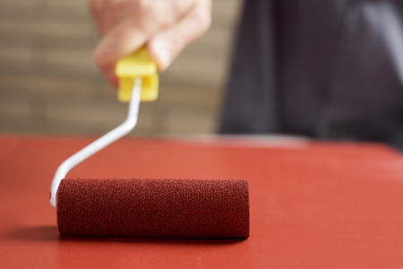 closeup of a young caucasian man in a working coat painting red a wooden board with a paint rollerの写真素材