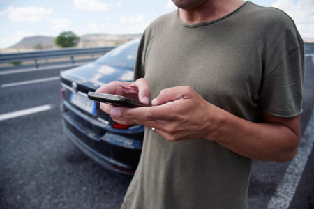 closeup of a young caucasian man wearing a t-shirt using a smartphone next to his car in a...