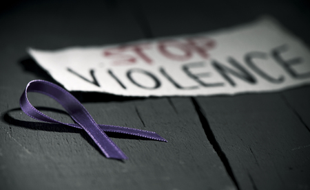 a purple ribbon for the awareness about the unacceptability of the violence against women and the text stop violence on a piece of paper, on a dark gray rustic wooden surfaceの写真素材