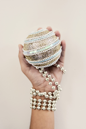an elegant christmas ball in the hand of a young caucasian man ornamented with a silvery beaded garlandの写真素材